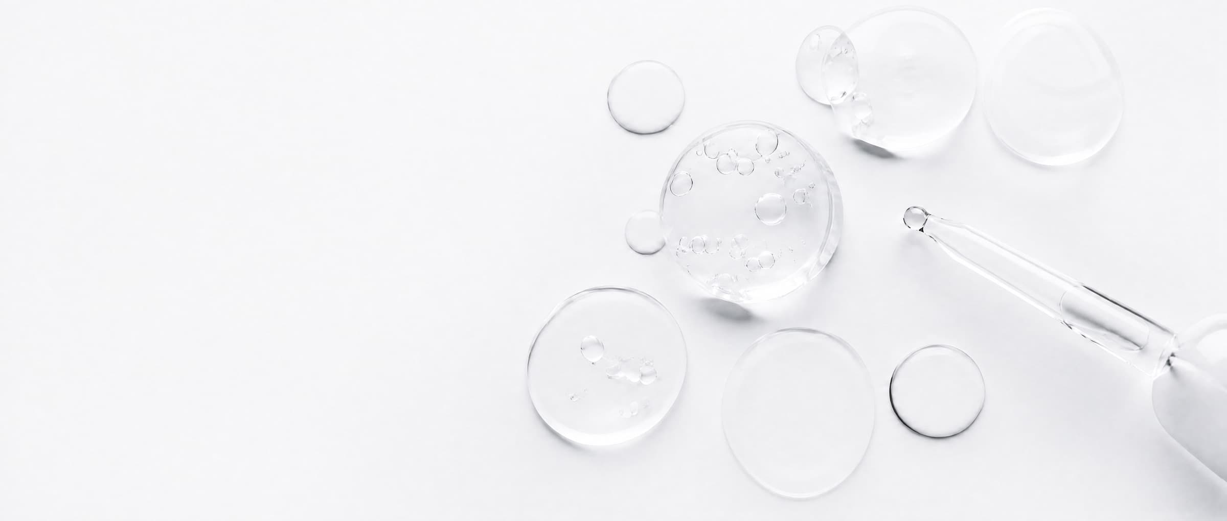 Clear liquid formulation droplets and a glass pipette on white — household-chemistry product development